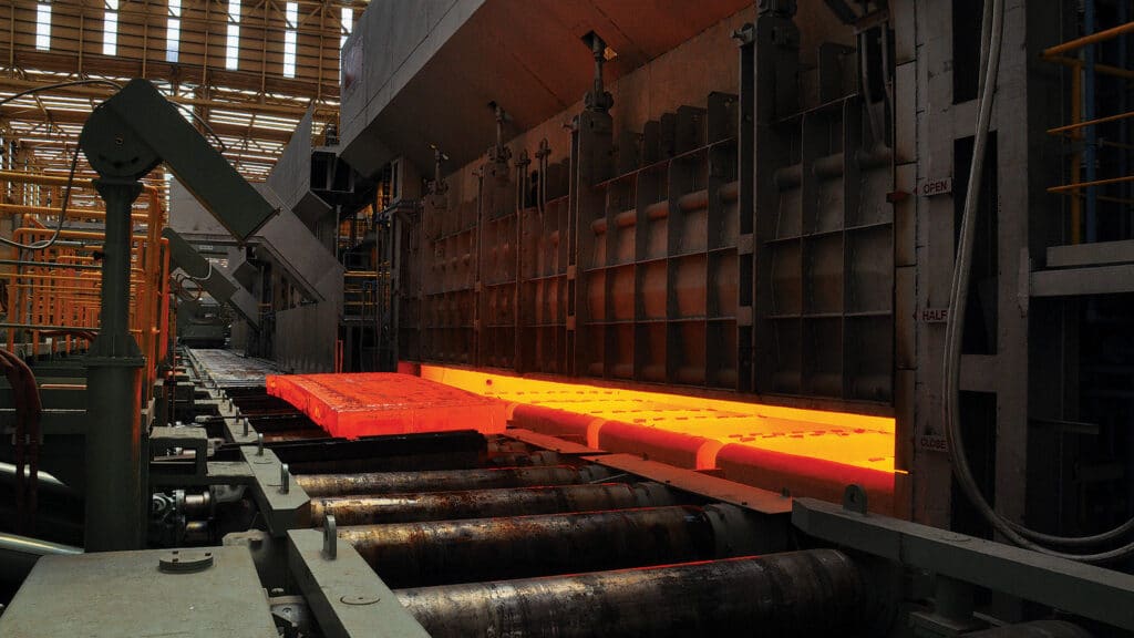 A red hot block of metal rolls down a conveyor in a steelworks factory.