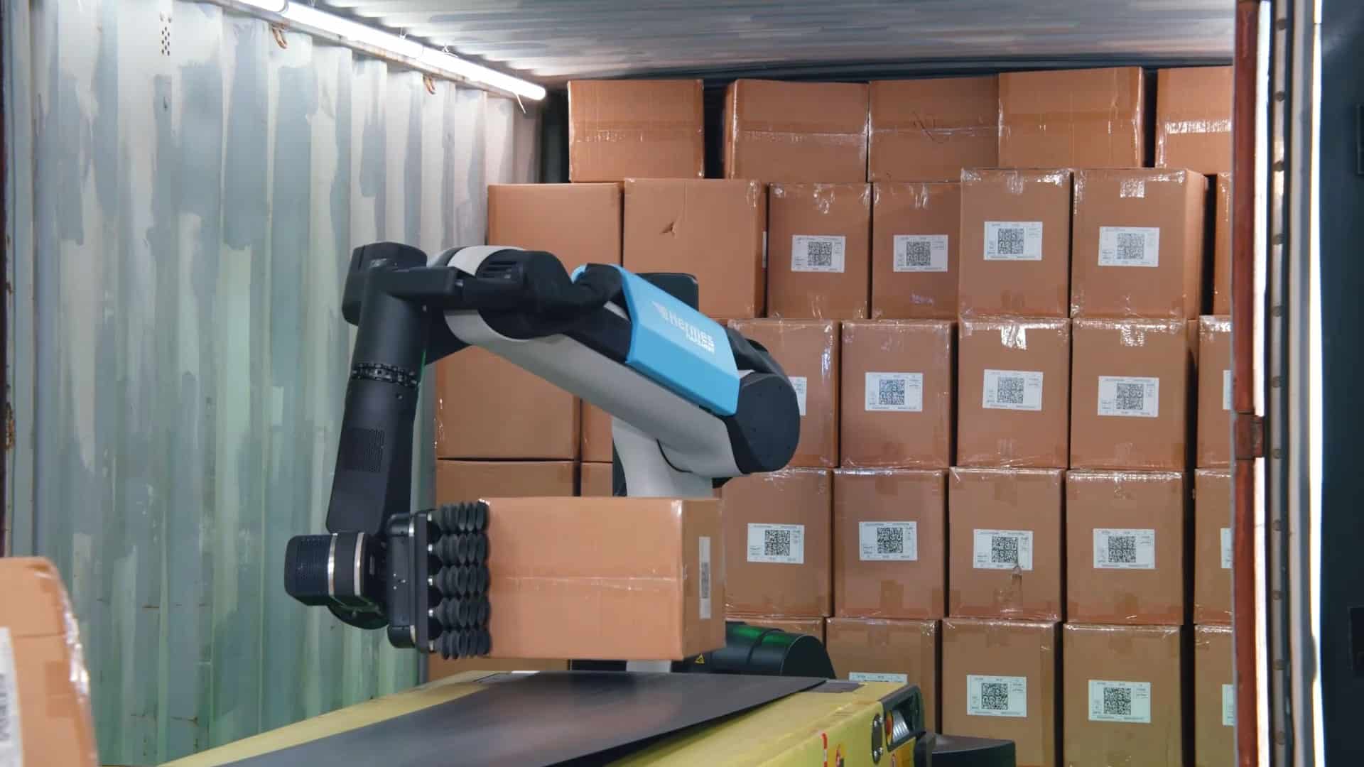 Robot bending its industrial arm grasps box inside container.