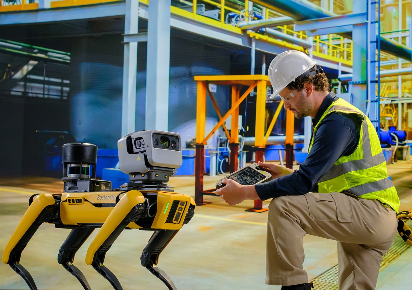 An operator kneels next to Spot in an industrial setting